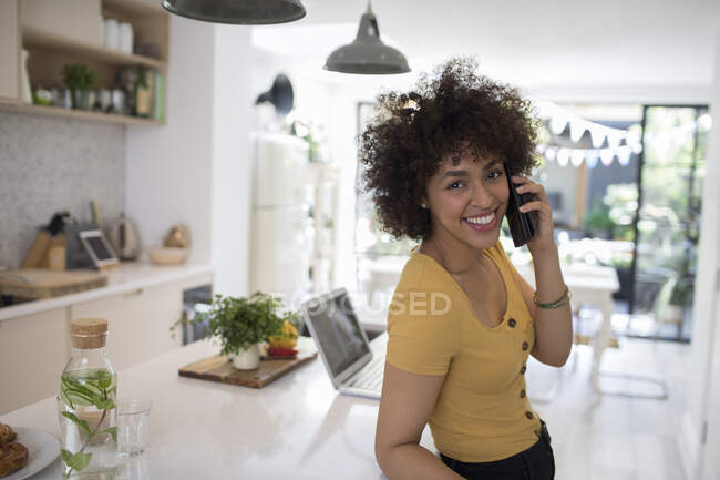 Portrait happy young woman talking on smart phone in kitchen — Stock Photo