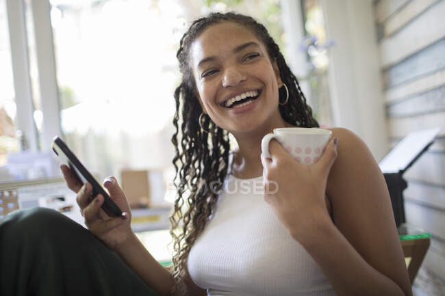 Portrait happy young woman with smart phone and tea laughing — Stock Photo