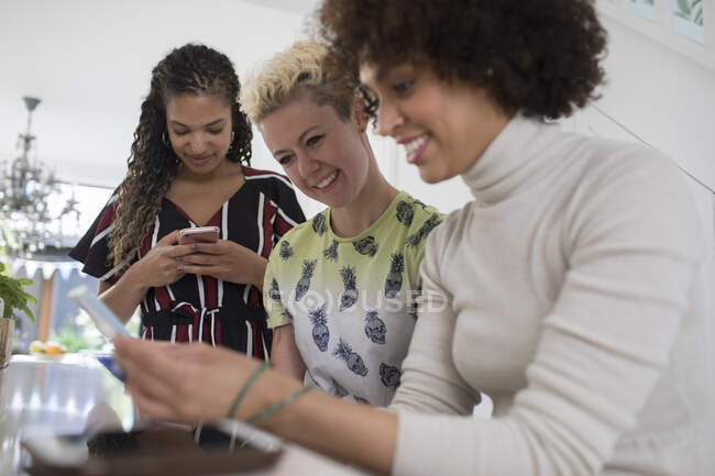 Young women friends using smart phones in kitchen — Stock Photo