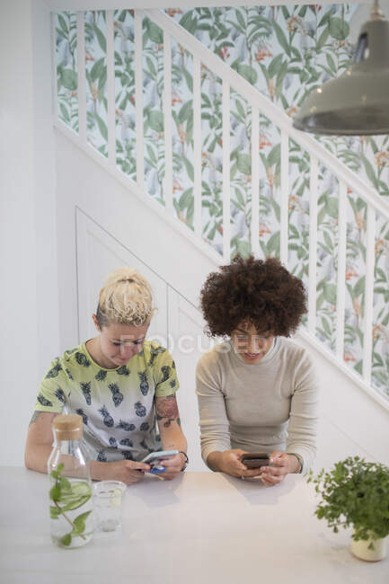 Молоді жінки друзі використовують смартфони на кухні — стокове фото