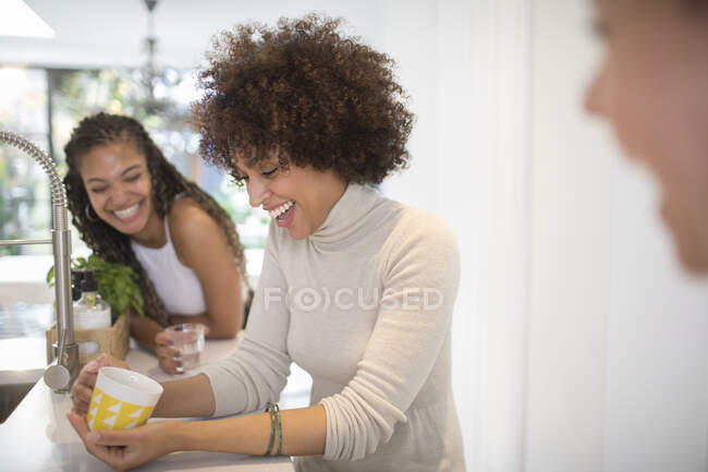 Happy young women friends laughing and drinking tea in kitchen — Stock Photo