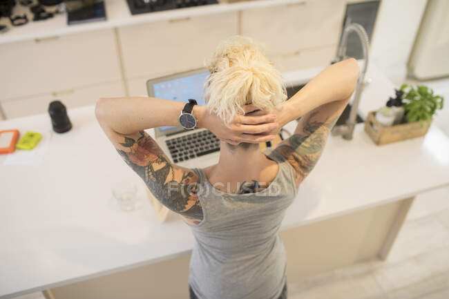 Jovem freelancer feminino com tatuagens trabalhando no laptop na cozinha — Fotografia de Stock