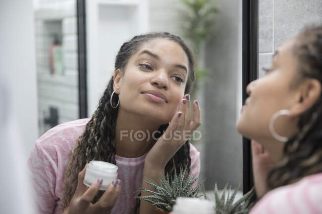 Beautiful young woman applying moisturizer in bathroom mirror — Stock Photo
