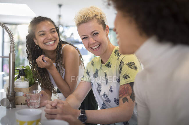 Счастливые молодые подруги смеются и разговаривают на кухне — стоковое фото