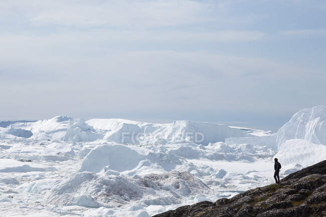 Man standing on cliff overlooking glacial ice melt Greenland — Stock Photo