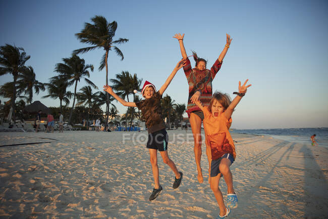 Retrato familiar despreocupado saltando de alegría en la playa tropical México - foto de stock