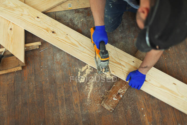 Carpintero de corte de madera con sierra en el sitio de construcción - foto de stock