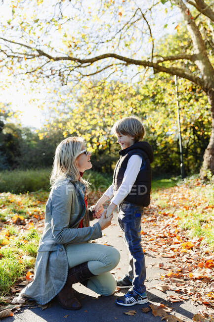 Mère et fils tenant la main et parlant dans un parc automnal ensoleillé — Photo de stock