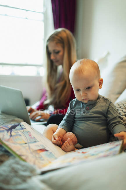 Carino innocente baby girl leggere il libro delle immagini a letto mentre la madre lavora — Foto stock
