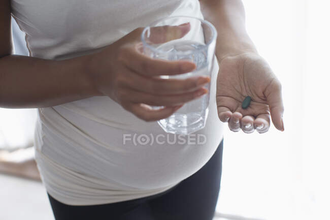 Cerca de la mujer embarazada que toma vitamina con agua - foto de stock