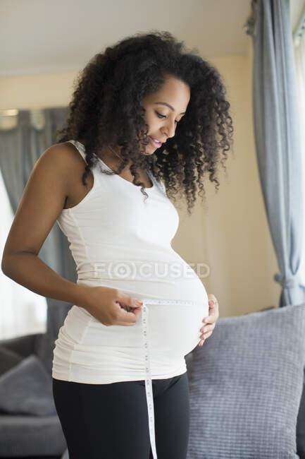 Mujer embarazada joven midiendo el estómago con cinta métrica - foto de stock