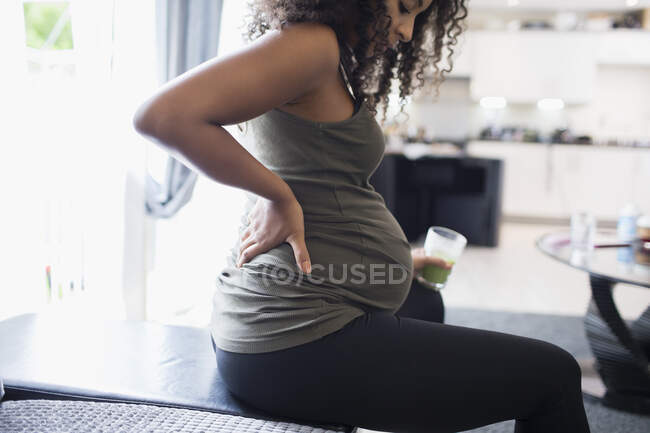 Young pregnant woman drinking green smoothie and holding back — Stock Photo