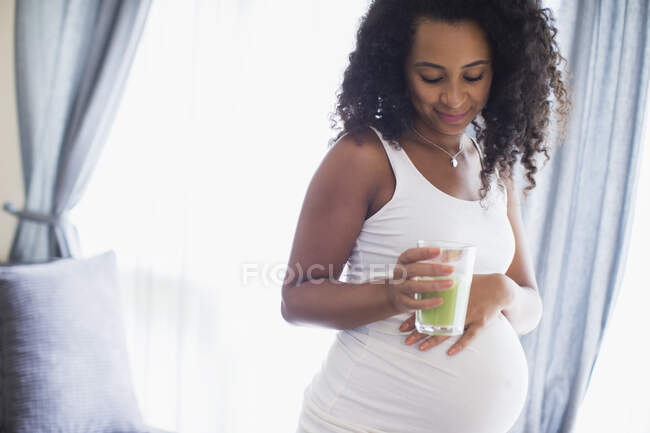 Jeune femme enceinte boire smoothie vert — Photo de stock