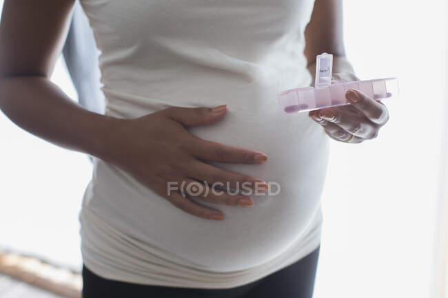 Молода вагітна жінка з коробкою таблеток приймає пренатальні вітаміни — стокове фото
