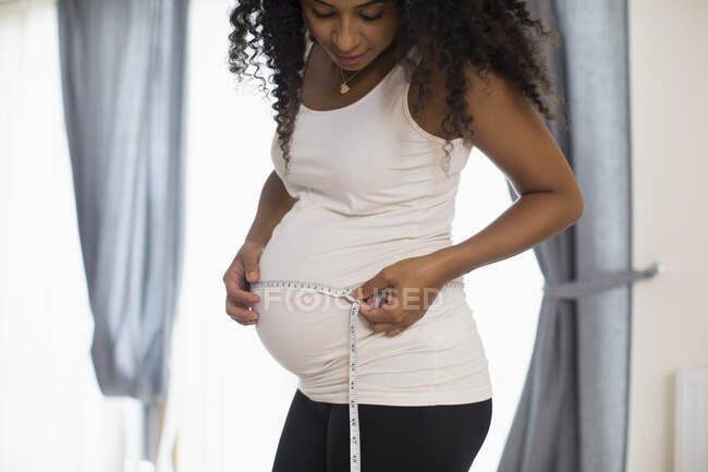 Mujer embarazada joven midiendo el estómago con cinta métrica - foto de stock