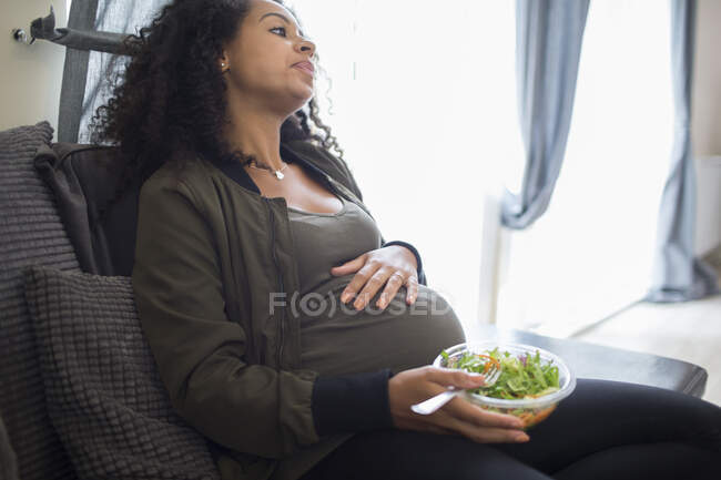 Уставшая молодая беременная женщина ест салат — стоковое фото