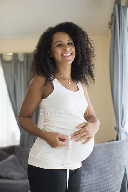Portrait happy young pregnant woman measuring stomach with tape measure — Stock Photo