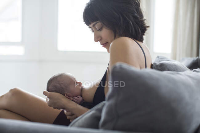 Mother breastfeeding newborn baby on sofa — Stock Photo