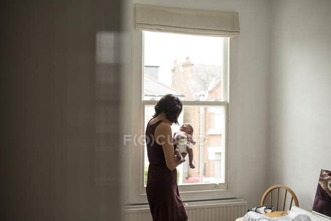 Mother holding innocent newborn baby boy at window — Stock Photo