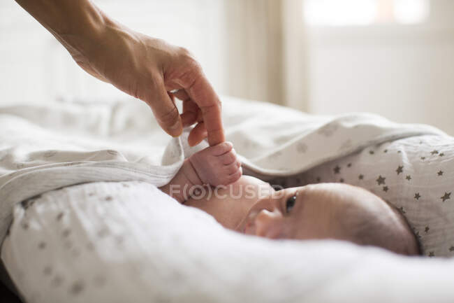 Mother holding hands with newborn baby boy laying in bassinet — Stock Photo
