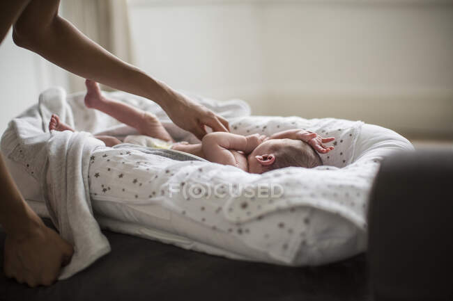 Mother reaching for newborn baby son in bassinet — Stock Photo