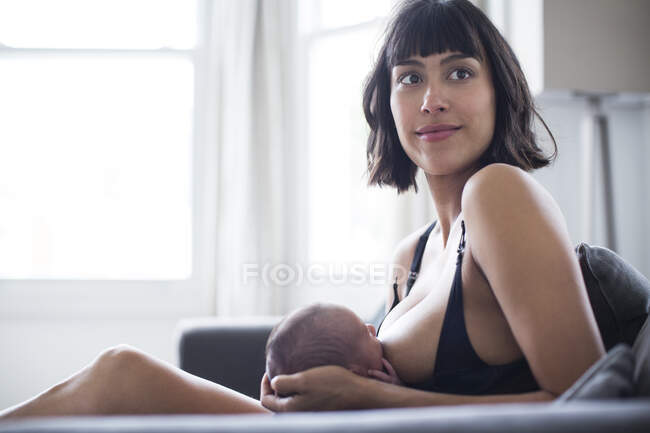 Retrato bela mãe amamentação recém-nascido bebê filho no sofá — Fotografia de Stock