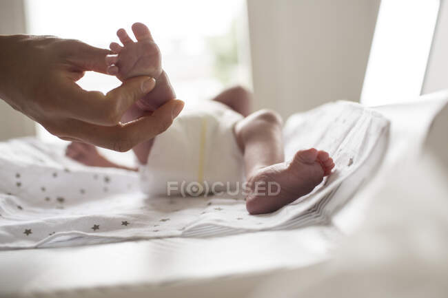 Mother holding tiny foot of newborn baby son laying on changing table — Stock Photo