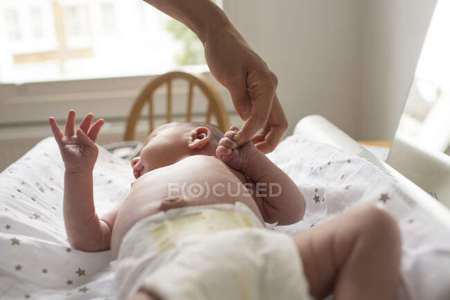 Mother holding hands with newborn baby son laying on changing table — Stock Photo