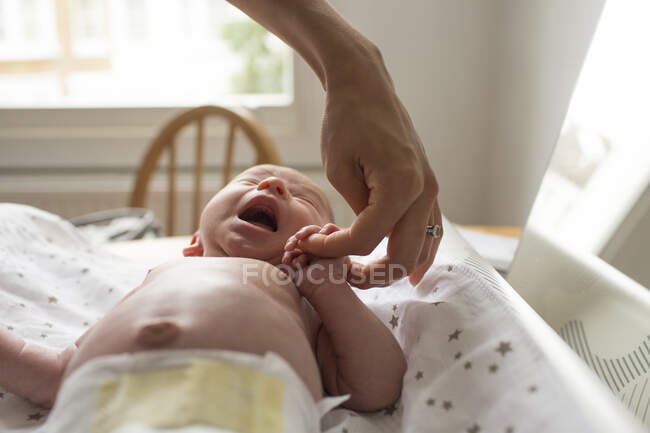 Mother holding hands with crying newborn baby son on changing table — Stock Photo