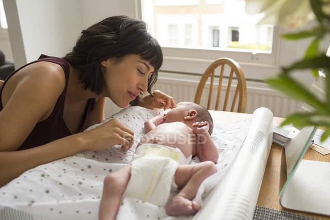 Loving mother watching newborn baby son laying on changing table — Stock Photo