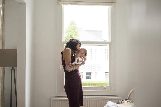 Mother kissing newborn baby son in window — Stock Photo