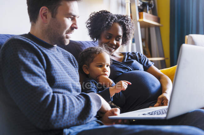 Familia multicultural con ordenador portátil en sofá - foto de stock