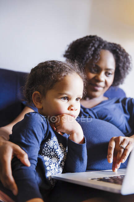 Pregnant mother and daughter using laptop — Stock Photo