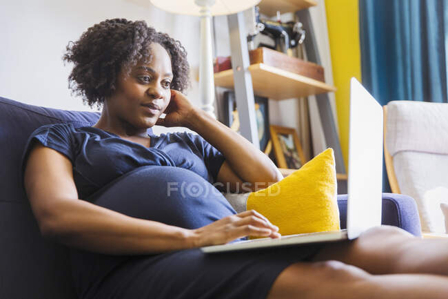 Mujer embarazadas que utiliza laptop en el sofá - foto de stock