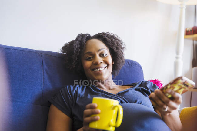 Portrait happy pregnant woman drinking tea and using smartphone — Stock Photo