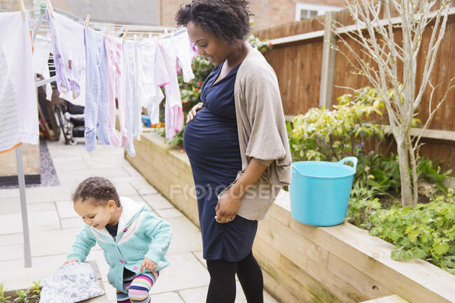 Pregnant mother and daughter hanging laundry on clothesline — Stock Photo