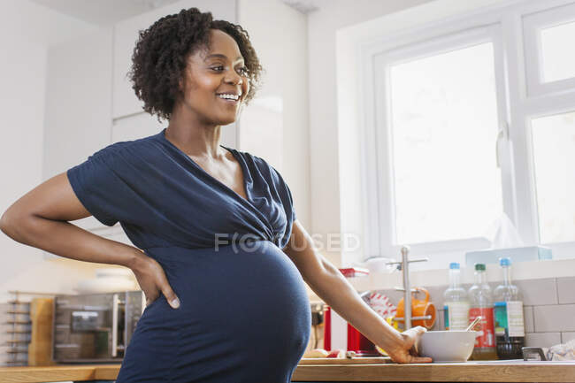 Feliz mujer embarazada comiendo en la cocina - foto de stock