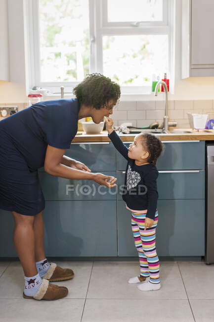 Симпатичная дочь кормит беременную мать на кухне — стоковое фото