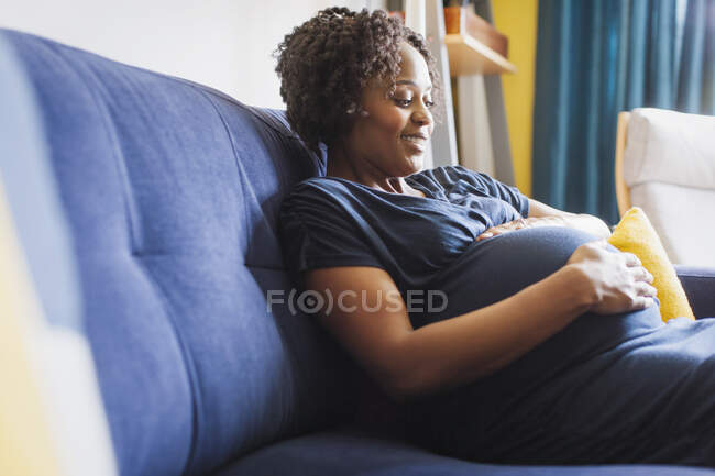 Счастливая беременная женщина трогает живот на диване — стоковое фото