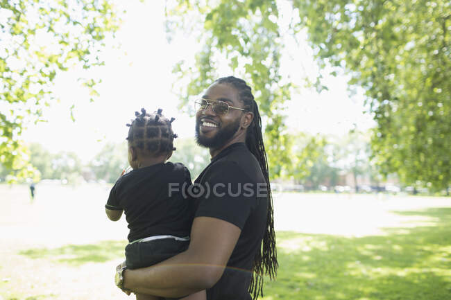 Портрет счастливого отца с длинными брейками, держащего маленького сына в парке — стоковое фото