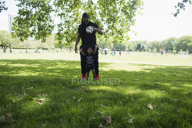 Padre e hijo menor jugando con balón de fútbol en el parque. - foto de stock