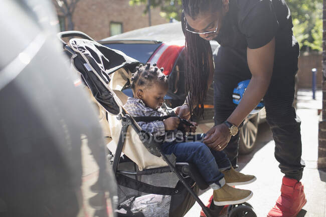 Батько кріплення маленького сина в колясці на сонячному тротуарі — стокове фото
