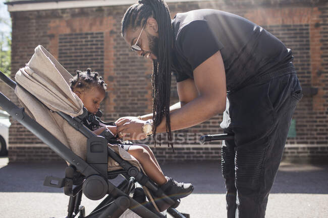 Padre fissaggio bambino figlio in passeggino sul marciapiede soleggiato — Foto stock