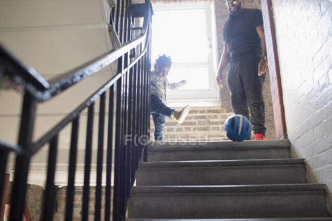 Padre e hijo menor jugando con el balón de fútbol en el aterrizaje de los establos - foto de stock