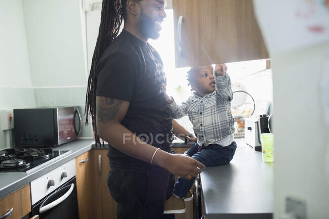 El padre y el hijo menor abren el armario en la cocina de los apartamentos. - foto de stock