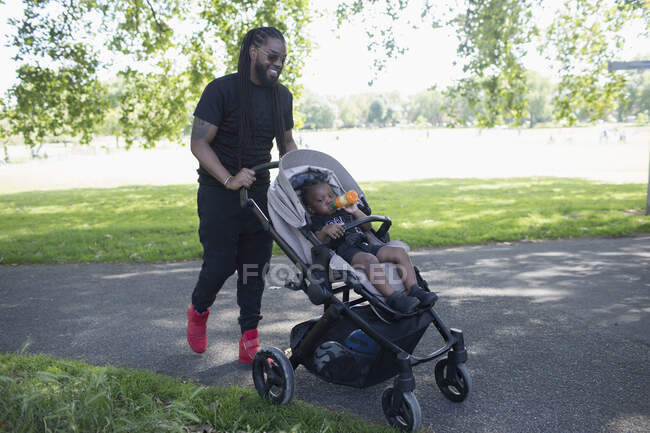 Отец толкнул маленького сына в прогулке в парке — стоковое фото