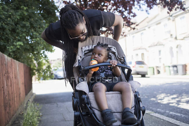 Père poussant un petit garçon dans une poussette sur un trottoir urbain — Photo de stock