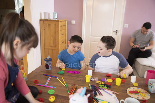 Niño con Síndrome de Down y hermanos jugando con juguetes en la mesa - foto de stock