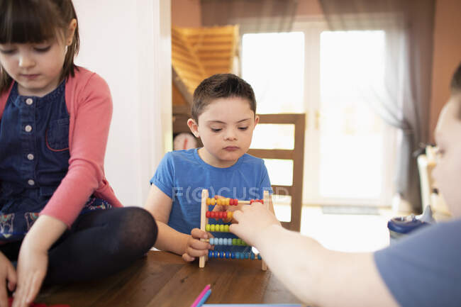 Niño con Síndrome de Down y hermanos jugando con juguete en la mesa - foto de stock