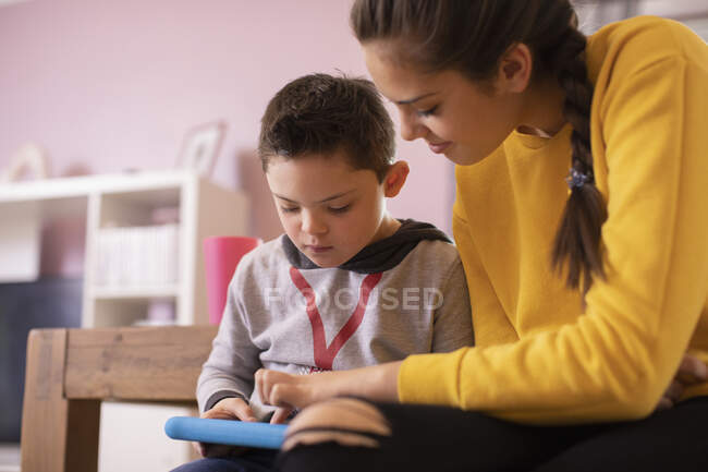 Sister helping brother with Down Syndrome using digital tablet — Stock Photo